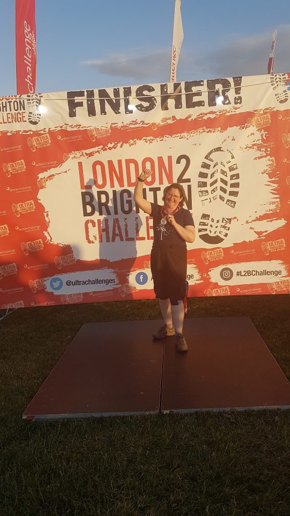 Me standing in front of a big Finisheer sign, holding my medal