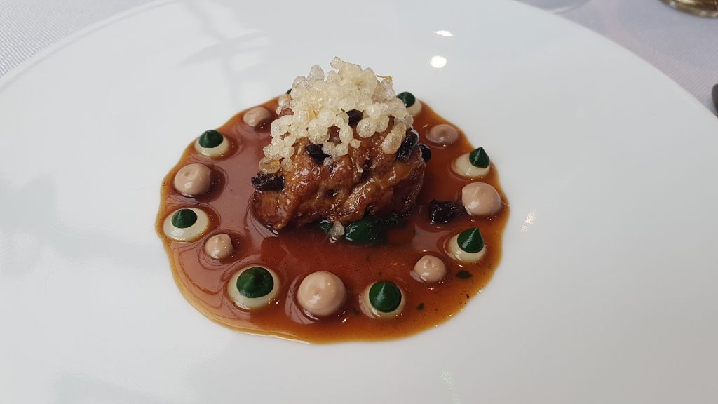 A sweetbread on a white place, with black and white dolups of puree and sauce