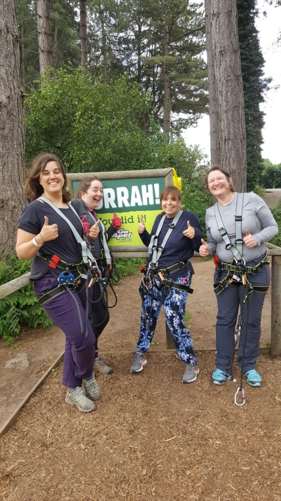 Four women wearing climbing harneses in the woods
