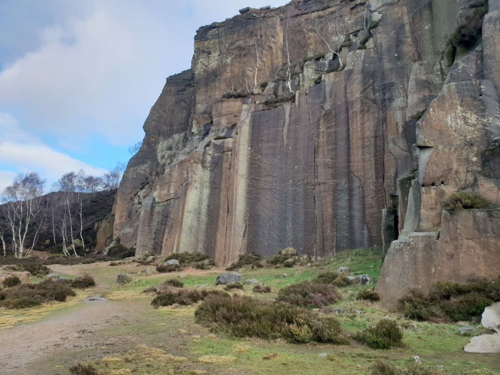 Sheer cliffs, a quarry in the Peak District. Blue sly and brown grass