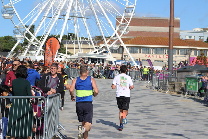Two runners heading towards finish with ferris wheel in background. 