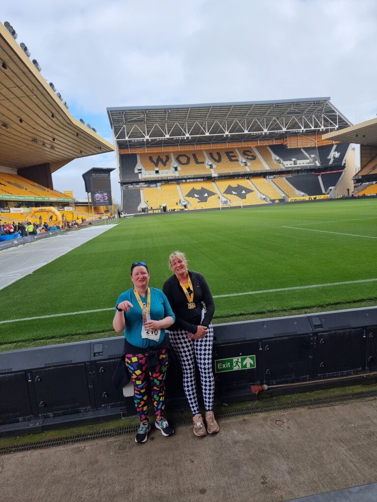 Myself and sister stanning in front of the Wolves football pitch with medals after our 10k run