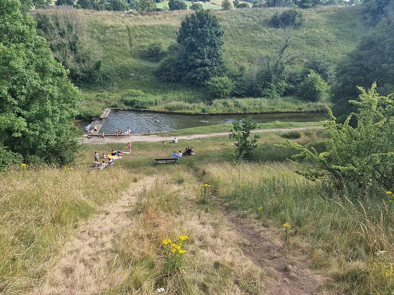 view down a hill to a river swimming pool, with children and parents all swimming