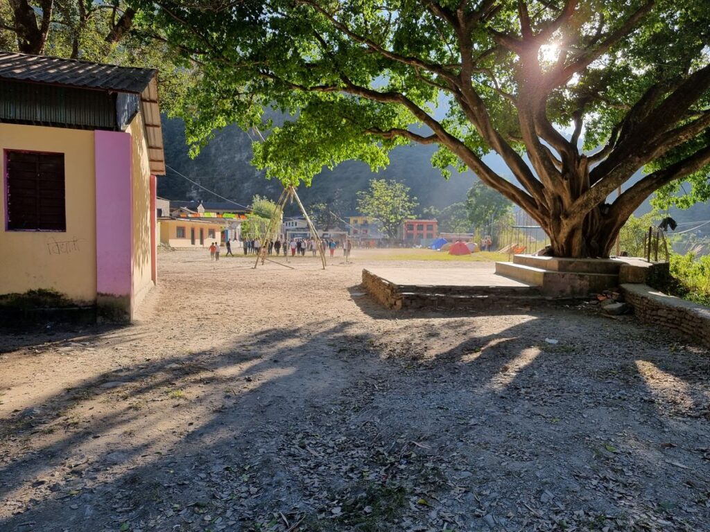 view of dirt school playground, with group of children being drilled in backlground and our tents by the side