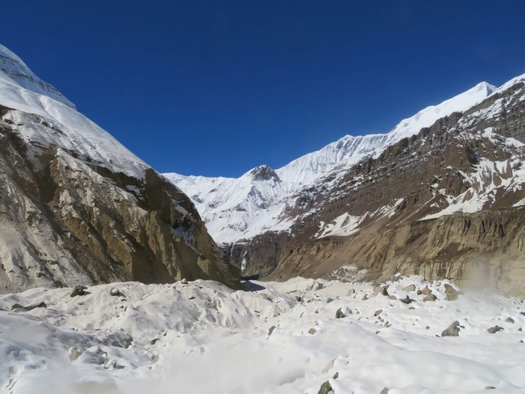 snow over glacial morrain, rocky slopes of mountains on both sides of the narrow valley