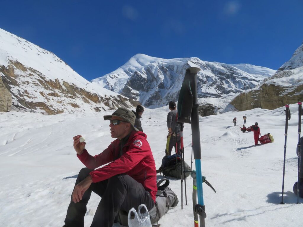 team sitting on bags on the snow, snowy valley in front with mountains behind