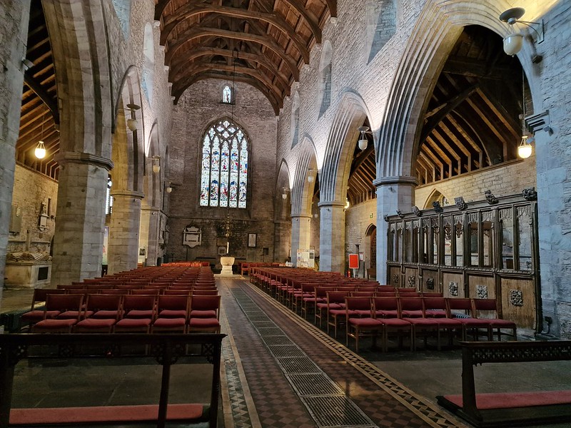 An image looking down the nave of Brecon Cathedral. Arches to each side, the font in the back before a stanined glass window